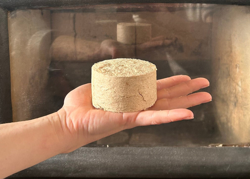 Hand holding a wood fire puck in front of a fireplace